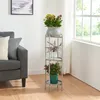 A plant stand with three potted plants next to a sofa and a window. Produktbild-Vorschau