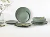 A collection of green stoneware plates and bowls are arranged on a white surface, with a sprig of eucalyptus in a glass vase to the left. Náhľad obrázku produktu
