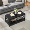 A black coffee table with items on it, placed in a living room setting next to a gray sofa. Produktbild-Vorschau
