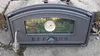 A cast iron pizza oven door with a glass window and thermometer, placed on a stone surface. Produktbild-Vorschau