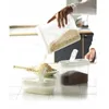A person is pouring dry goods from a clear plastic container into another container on a kitchen counter. Produktbild-Vorschau