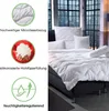A bed with white bedding, pillows, and a bolster, set against a backdrop of a city skyline at night visible through large windows. Produktbild-Vorschau
