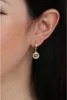 Close-up of a woman's ear wearing a gold earring with a circular pendant adorned with small stones. Anteprima dell’immagine prodotto