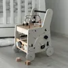 A wooden baby walker with various activity toys is placed on a wooden floor next to a crib. Produktbild-Vorschau