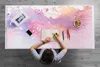A person is drawing on a notebook placed on a desk with a watercolor-like pattern. The desk also has a phone, a picture frame, colored pencils, and a bowl of snacks. Produktbild-Vorschau