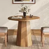 A round wooden dining table with a vase of flowers and two candles on it, placed on a rug with two chairs on either side. Produktbild-Vorschau