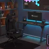 A gaming setup with a chair, desk, computer, and accessories, illuminated by colorful LED lights. Produktbild-Vorschau