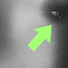 A bright green arrow points to a cluster of small, bright objects in the upper right corner of a gray, textured background. Produktbild-Vorschau