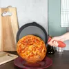 A cast iron pan with a round bread or cake inside, being held by a hand with a red silicone grip, on a kitchen counter with cutting boards and a bottle of oil. Produktbild-Vorschau