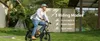 A man is riding an electric bicycle on a paved path surrounded by greenery and modern architecture. Produktbild-Vorschau