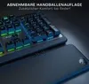 A close-up view of a gaming keyboard with RGB lighting, with a dark background and a detached wrist rest in the foreground. Produktbild-Vorschau