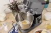 A kitchen scene with a stand mixer, ingredients, and baking tools on a wooden table. Podgląd zdjęcia produktu