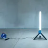 A vertical LED work light on a tripod is connected to a corded reel, set up on a concrete floor in front of a concrete wall. Náhled obrázku produktu
