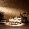 A wooden model of a steam locomotive is displayed on a wooden surface with a wooden wall in the background. An old-fashioned telephone and a vintage radio are also visible. Náhľad obrázku produktu