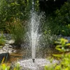 A fountain spraying water in a pond surrounded by greenery and rocks. Produktbild-Vorschau