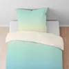 A duvet cover and pillowcase set with a gradient color pattern is laid out on a bed. Produktbild-Vorschau