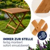 A wooden folding table is set up on a grassy lawn next to a pond. Produktbild-Vorschau
