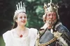 A young woman in a white dress and crown stands next to an older man in royal attire, both wearing crowns. Náhled obrázku produktu
