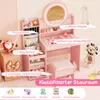 A pink children's vanity set with a mirror, stool, and storage shelves, decorated with various accessories and toys. Voir les images du produit
