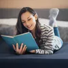 A woman is lying on a bed, reading a book. Náhľad obrázku produktu