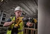 A construction worker is using a Dewalt hammer drill on a concrete pillar. Produktbild-Vorschau