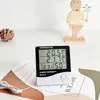 A digital thermometer and hygrometer sits on a surface with decorative items in the background. Anteprima dell’immagine prodotto