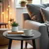 A round side table with a plant and a cup of coffee next to a sofa. Náhľad obrázku produktu