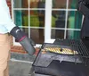 A person wearing a BBQ glove is grilling a fish on a grill. Produktbild-Vorschau