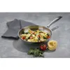 A stainless steel frying pan filled with pasta, tomatoes, and spinach, placed on a gray surface next to a folded gray towel, a tomato, and a nest of pasta. Podgląd zdjęcia produktu