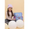 A young girl sits on the floor next to a backpack, with large white balloons in the foreground. Produktbild-Vorschau