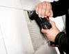 A person is using a Metabo multitool to remove grout from between tiles on a wall. Náhľad obrázku produktu