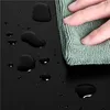 A hand is wiping water droplets off a black surface with a green microfiber cloth. Produktbild-Vorschau