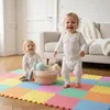 Two babies playing on a colorful puzzle mat in a living room. Produktbild-Vorschau