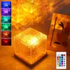 A cube-shaped lamp with a textured surface is shown in the center, projecting a warm, wavy light pattern onto the background. A small remote control is visible in the lower right corner. A collage of smaller images showing the lamp in different colors is o Produktbild-Vorschau