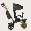 A black Lionelo Kori tricycle with a gold handle and canopy, shown against a plain light beige background. Produktbild-Vorschau