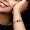 A close-up shot of a woman's arm wearing a Pandora bracelet with a red heart charm. Produktbild-Vorschau