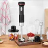 A black and silver immersion blender with accessories is displayed on a wooden countertop next to a checkered towel and kitchen tiles. Produktbild-Vorschau
