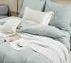 A neatly made bed with light blue bedding, decorative pillows, and a white knitted throw blanket. Produktbild-Vorschau