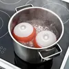 Two red and white spherical objects with white tops are boiling in a pot of water on a black stovetop. Podgląd zdjęcia produktu