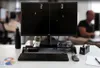 A desk setup with a computer monitor displaying a game of Pong, a keyboard, mouse, and other office supplies. Produktbild-Vorschau