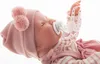 A close-up of a baby doll wearing a pink hat and outfit, with a pacifier in its mouth. Anteprima dell’immagine prodotto