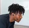 A man with dreadlocks wearing black earbuds and a black t-shirt, looking to the side. Produktbild-Vorschau