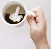 A hand holding a white mug filled with dark liquid, with a white ceramic middle finger sculpture inside. Produktbild-Vorschau