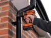 A person is using a Black & Decker cordless drill to drill a hole in a downspout attached to a brick wall. Produktbild-Vorschau