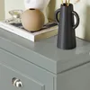 A close-up view of a gray dresser with decorative items on top, including a book, a vase, and a candle holder. Podgląd zdjęcia produktu