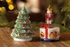 Two Christmas-themed ceramic figurines, a Christmas tree and a nutcracker on a gift box, are displayed on a wooden surface. Náhled obrázku produktu