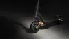 A close-up, studio shot of a black electric scooter with gold accents, set against a dark, shadowed background. Produktbild-Vorschau