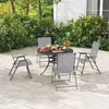 A patio set with a round table and four chairs on a paved patio surrounded by greenery. Produktbild-Vorschau