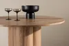 A close-up of a round wooden table with two glasses and a black bowl on it. Produktbild-Vorschau