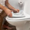 A person is placing a child's toilet seat onto a toilet. Produktbild-Vorschau